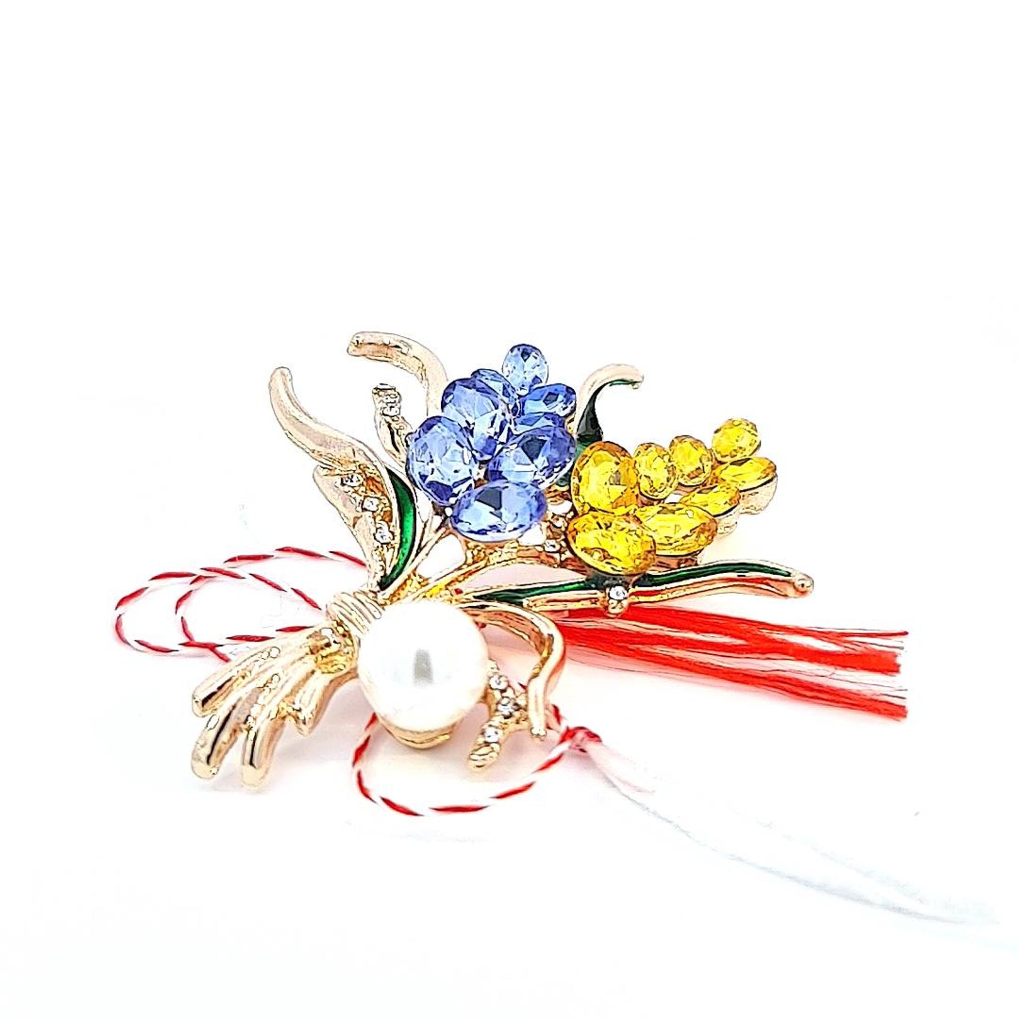 Close-up of the 'Pearlescent Harmony' Martisor brooch, displaying blue and yellow crystals with a central faux pearl.