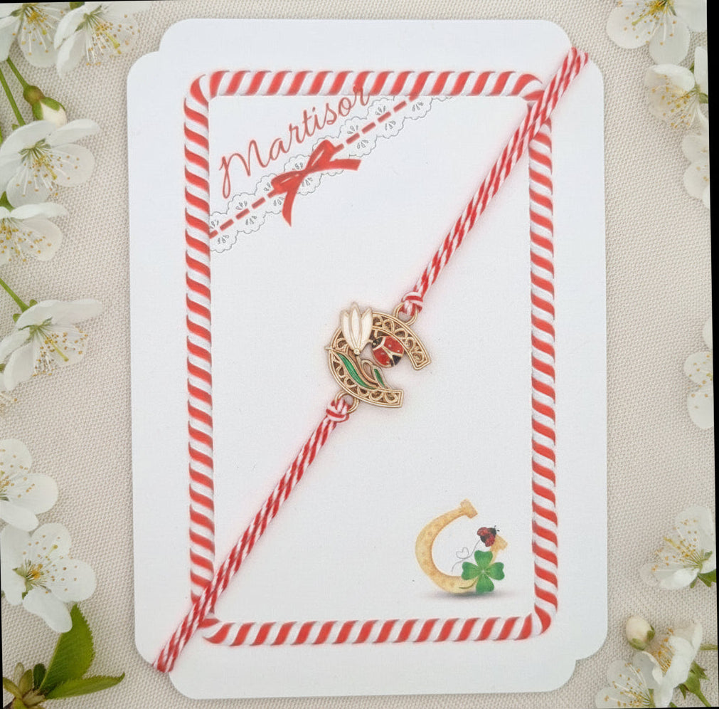 Horseshoe, snowdrop and ladybird Mărțișor bracelet displayed on bilingual story card with red and white frame