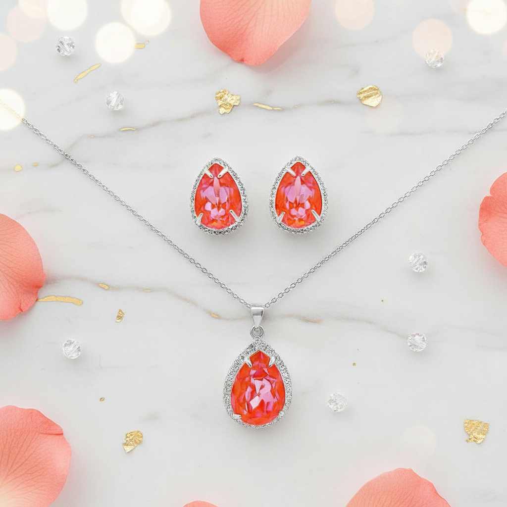 Sterling silver jewellery set with pear-shaped orange Delite crystals, including matching stud earrings and large pendant, styled on marble background with petals – Magpie Gems.