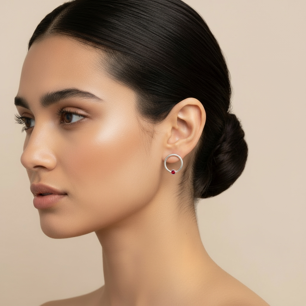 Woman wearing a silver hoop earring with a red gemstone, a minimal and elegant design, featuring a small red birthstone accent at the base of each circle