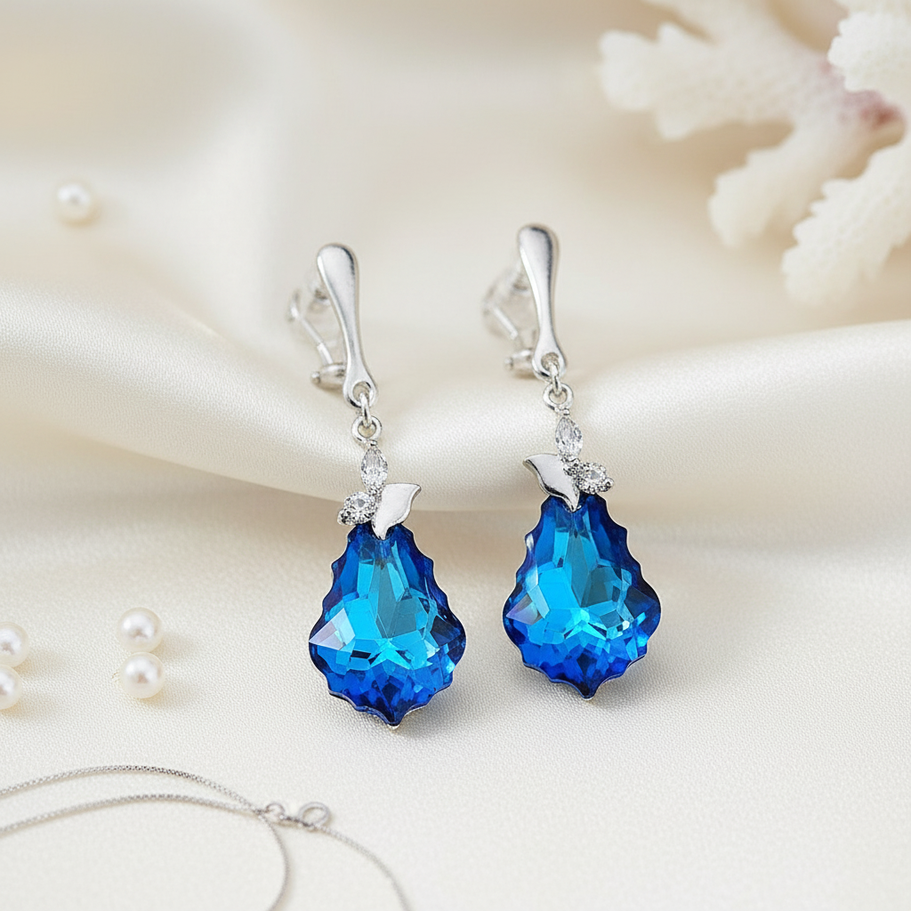 Sterling silver statement drop earrings with deep blue faceted crystal baroque teardrops and delicate butterfly detailing, handcrafted by Magpie Gems.