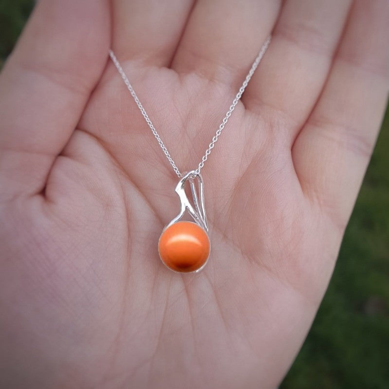 Hand holding a Coral Crystal pearl luster necklace on a sterling silver chain from Ireland