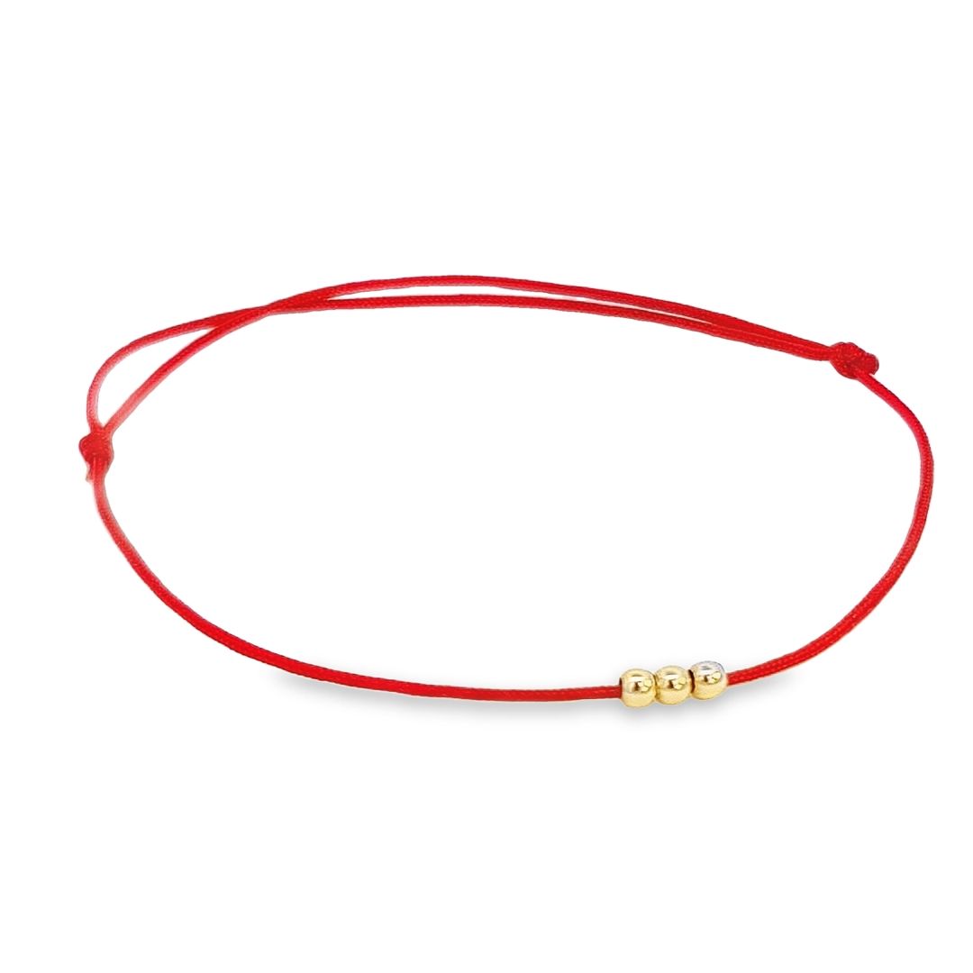 Three 14k solid gold beads aligned on Magpie Gems' 'Trio of Harmony' Bracelet, set against a vivid red string backdrop.