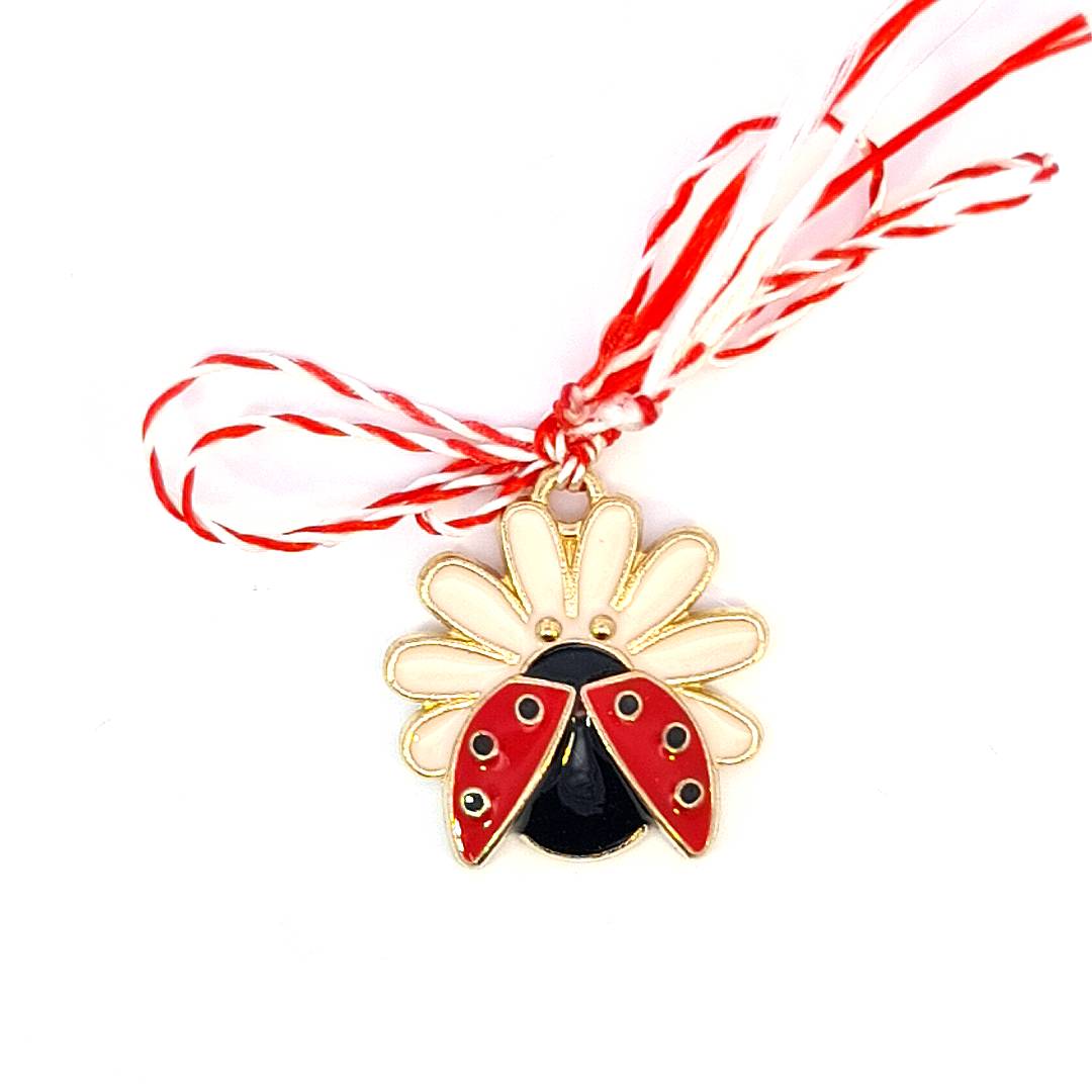 A gold and red ladybug charm with peach enamel petals, attached to a Martisor red and white twisted string, ready for the springtime gifting season.