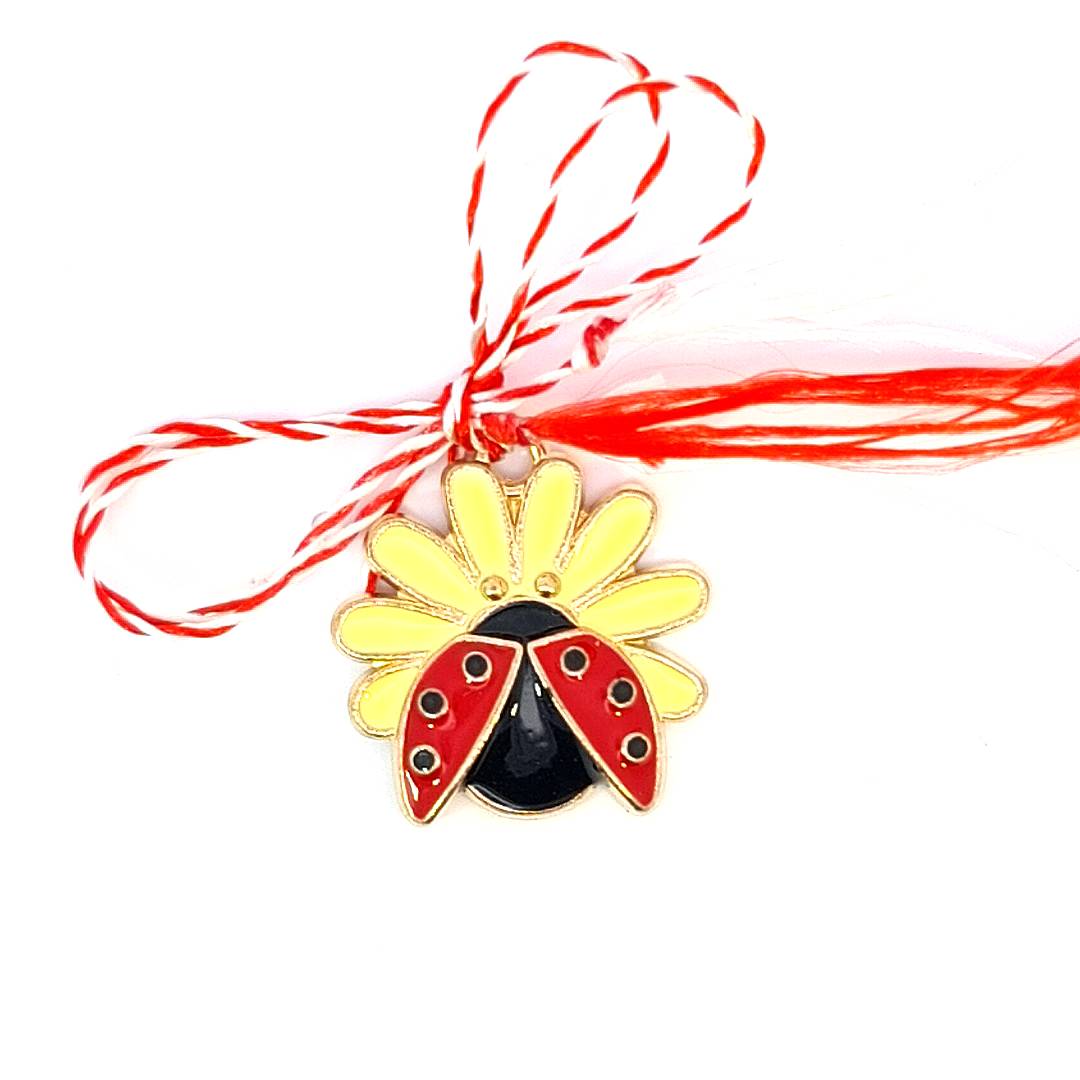 Red and white Martisor string tied around a gold-plated ladybug charm with yellow enamel daisy accents for spring celebration.
