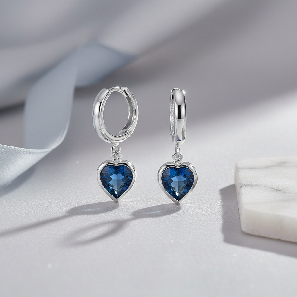 Sterling silver hoop earrings with Montana blue heart December birthstone charms, displayed in elegant flatlay – Magpie Gems.