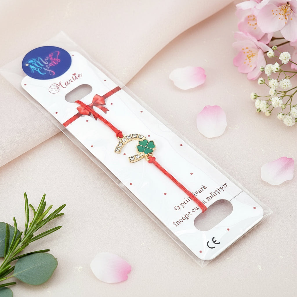 Gold-plated horseshoe and green enamel four-leaf clover Martisor Bracelet with red adjustable macramé cord, displayed on a presentation card.
