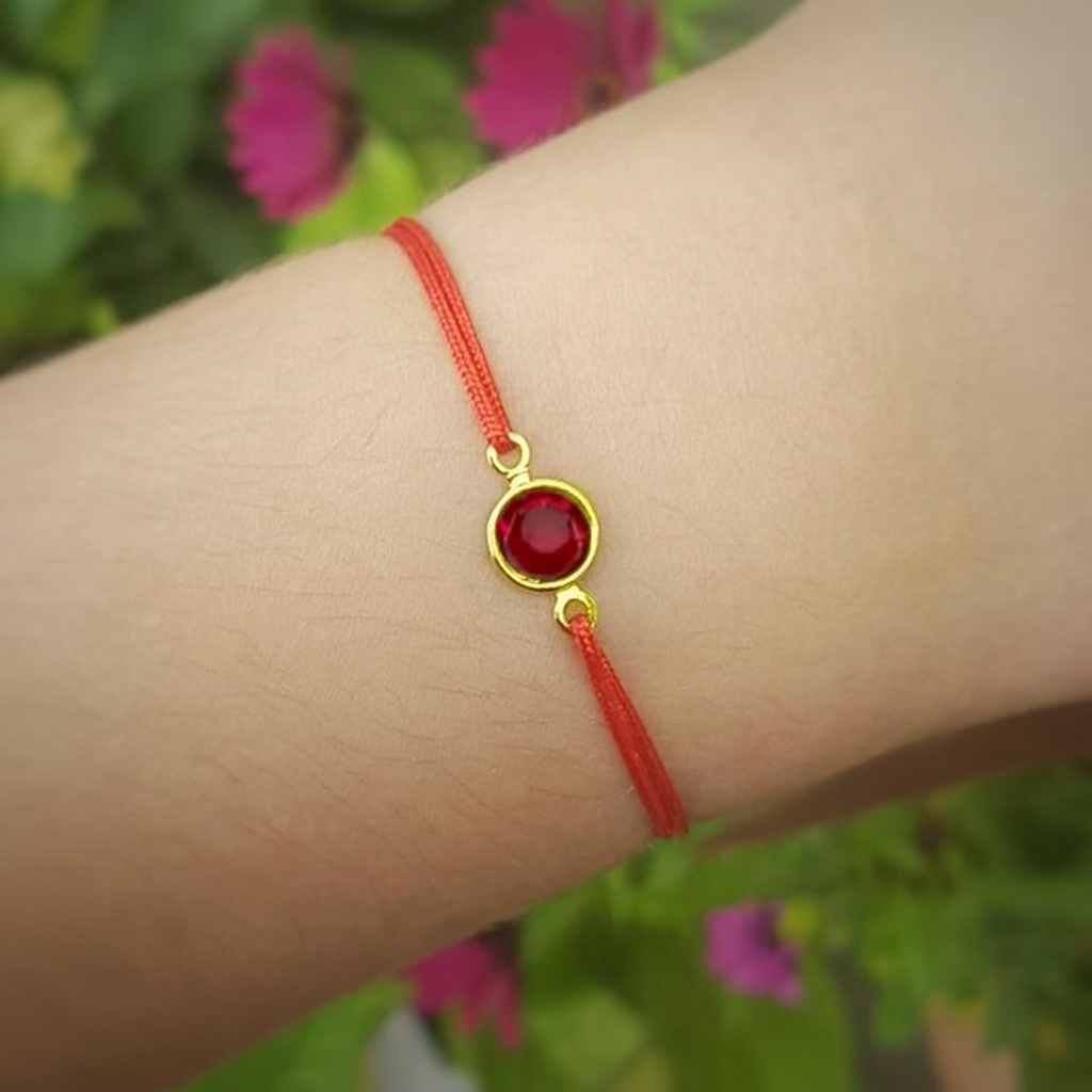 Red string bracelet with a gold siam red as January Birthstone on a wrist against a blurred natural background