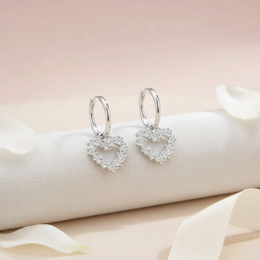 Heart-shaped silver earrings on a white cushion with a soft pink background