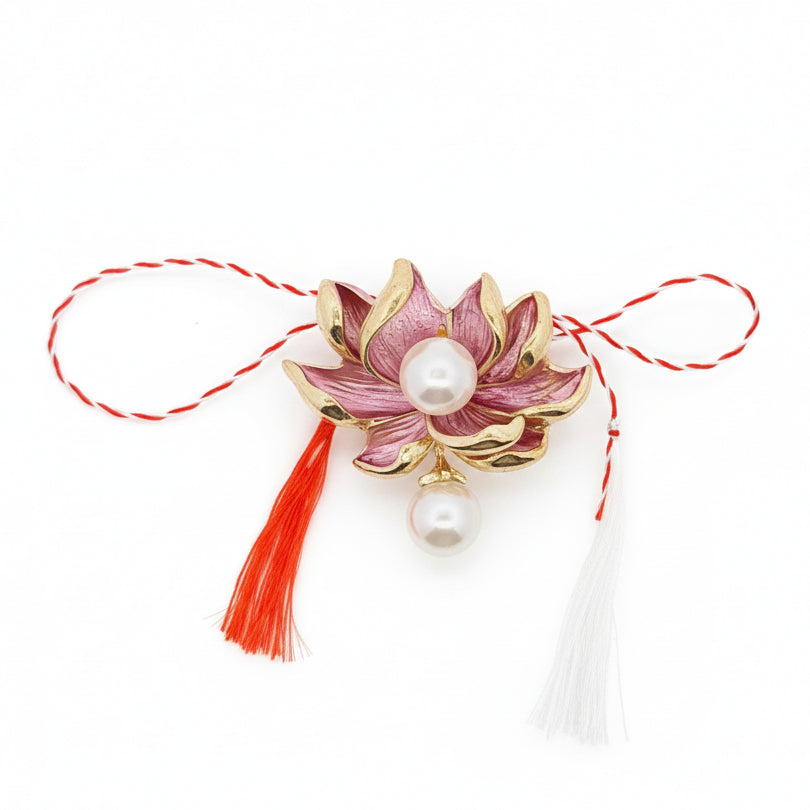Decorative brooch with pink lotus flower design, pearls, and Martisor tassels on a black background