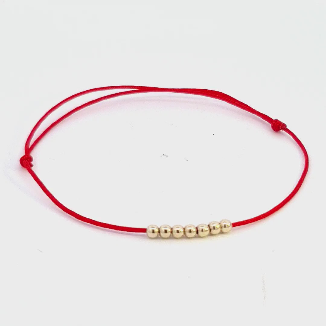Captivating 45-degree rotational video of the Sevenfold Path – 14k Gold Bead Bracelet, presenting all seven 14k solid gold beads on a symbolic red string.