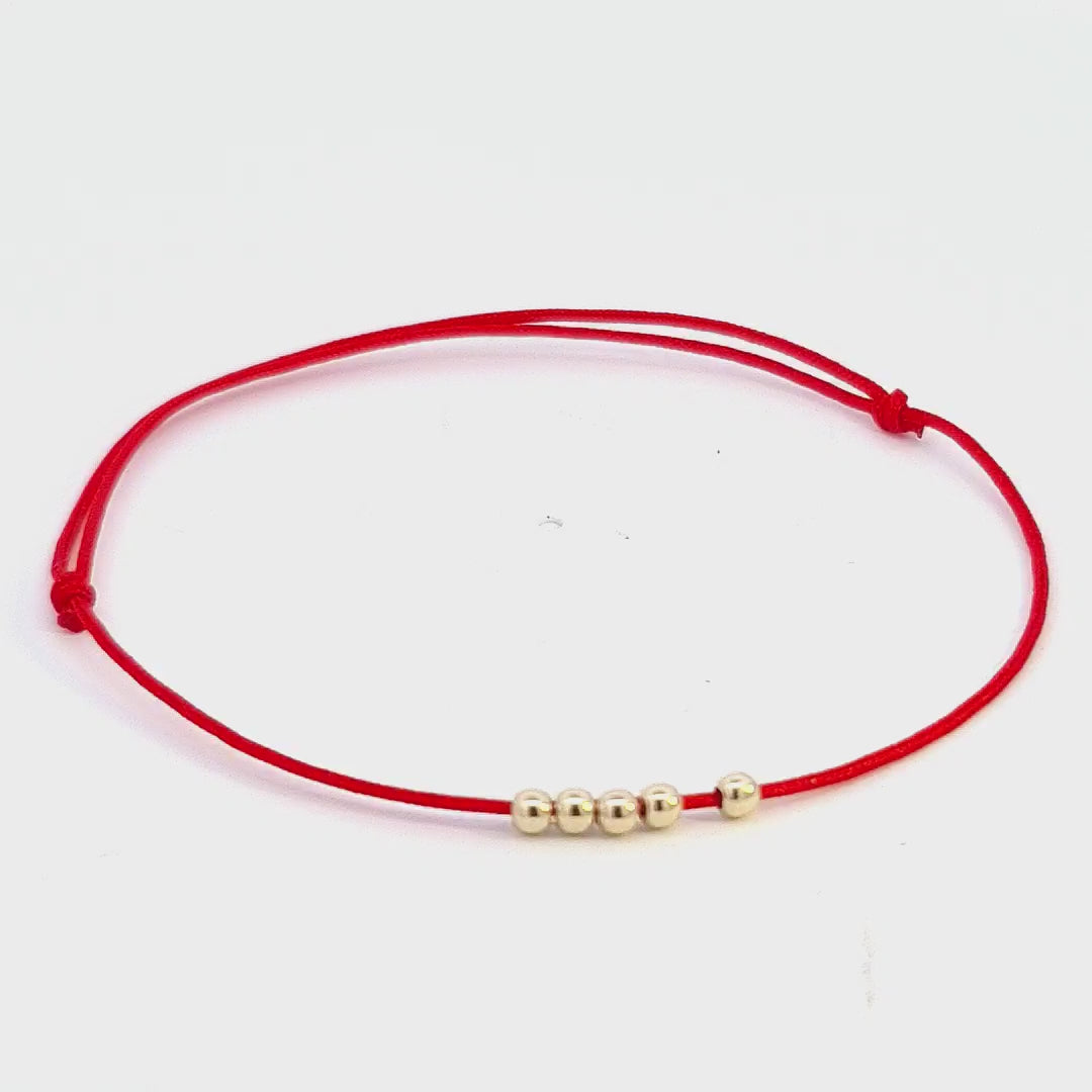 Elegantly rotating view of the 'Quintessence Circle' Bracelet, displaying the five 14k solid gold beads on an adjustable red string.