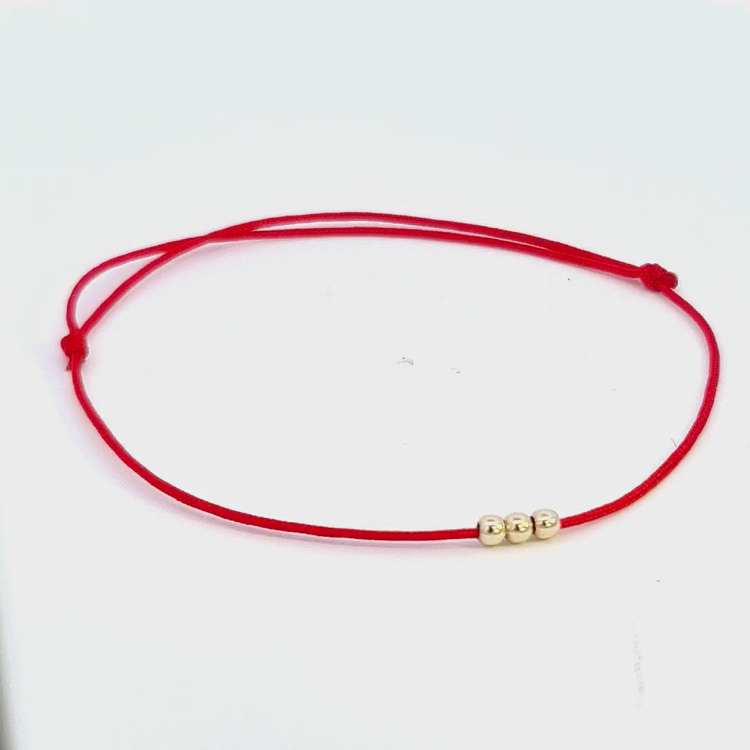 Video showcasing the 'Trio of Harmony' Bracelet from Magpie Gems in Ireland, rotating to display the triad of 14k solid gold beads on the red string.