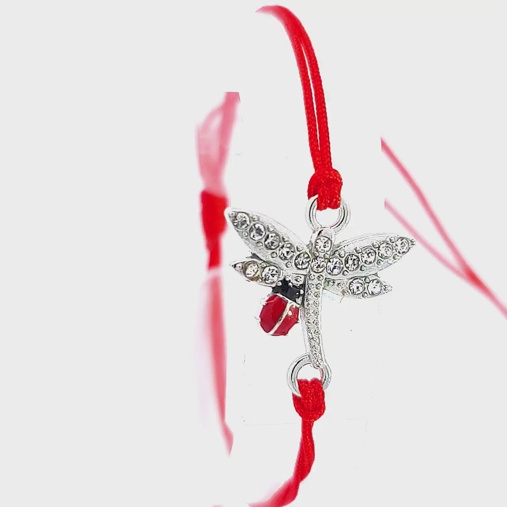 Presentation video of the 'Whispers of Spring' Martisor Bracelet, focusing on the sparkling dragonfly charm and the vibrant ladybird against the red cord, set on a white surface for contrast.