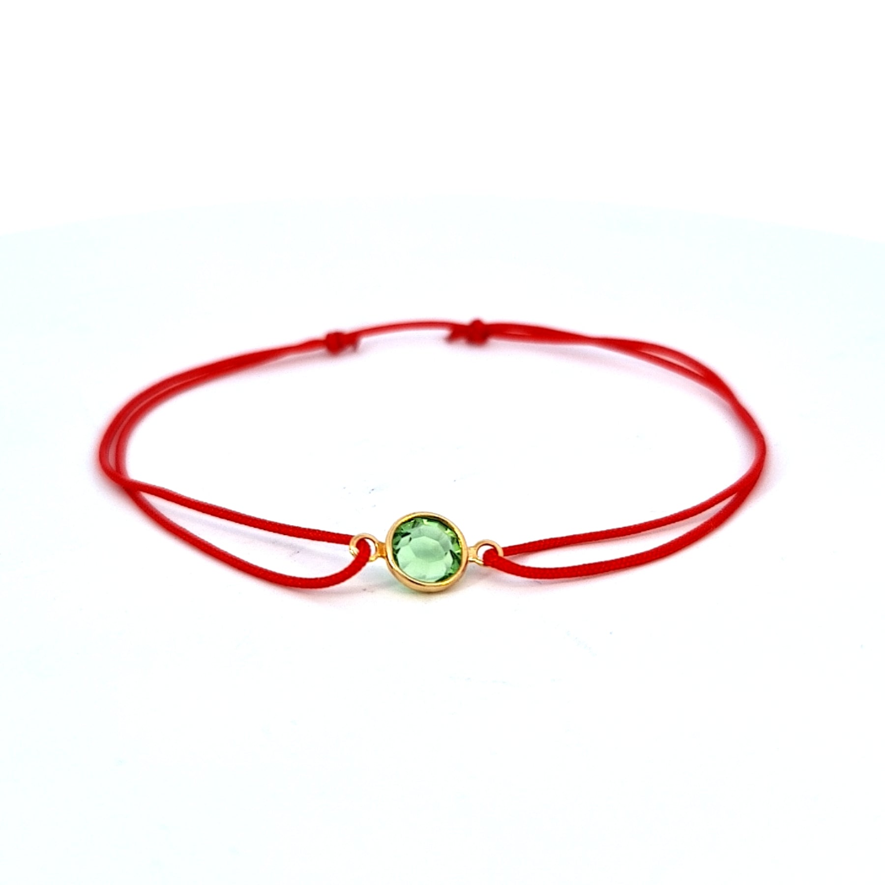 Red bracelet with a peridot green gemstone as August birthstone on a white background