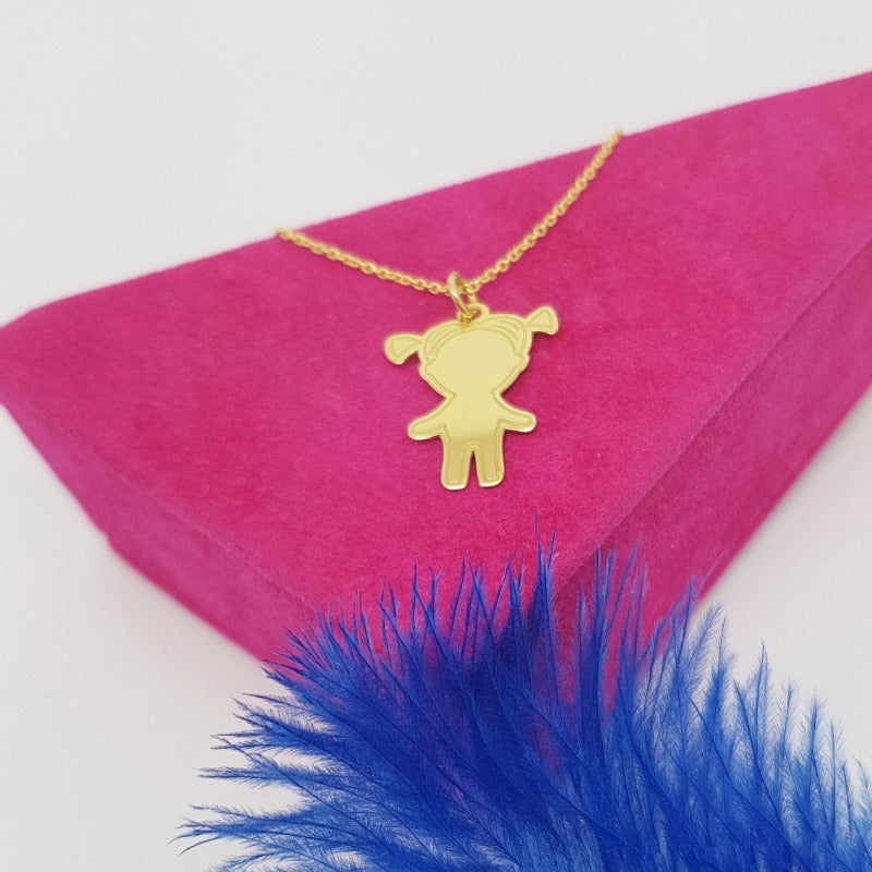 Charming Little Girl Pendant Necklace in 24k gold plating, laid on vivid pink velvet next to vibrant blue feathers, showcasing a playful and colourful presentation by Magpie Gems Ireland