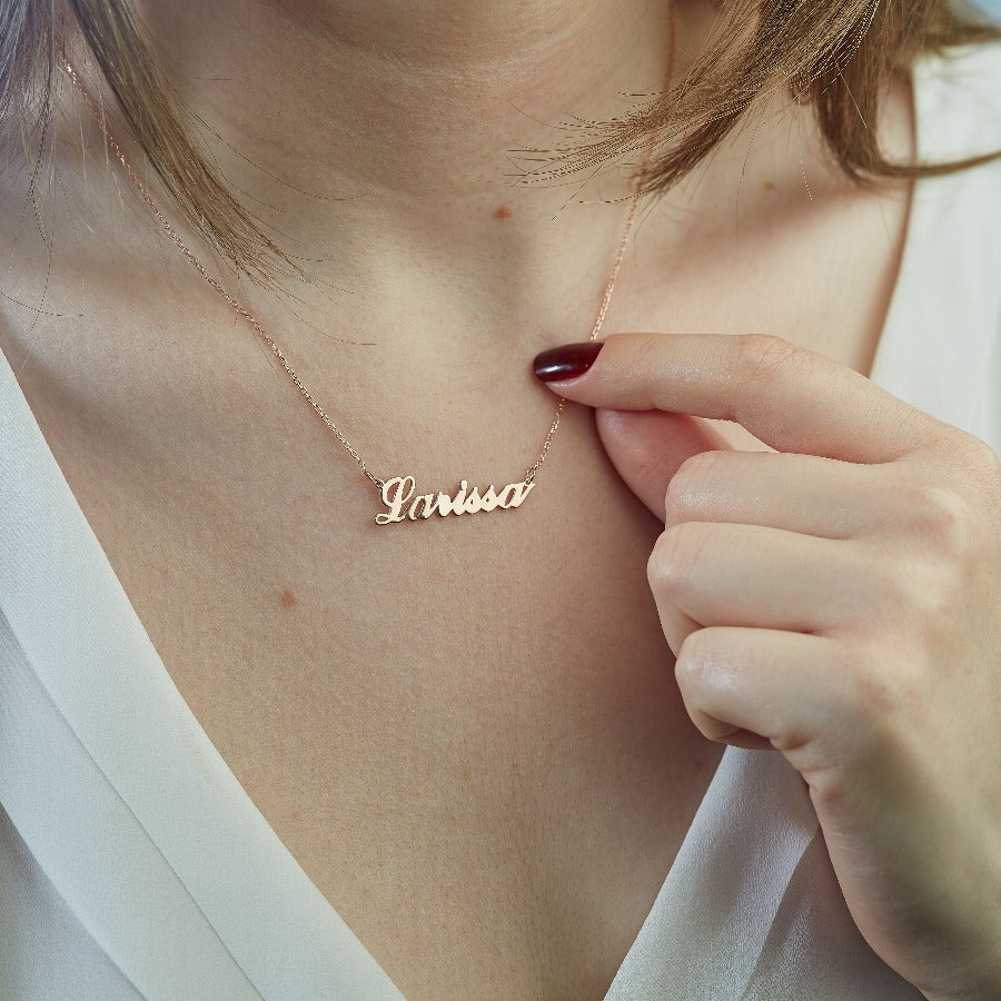 Image of a woman wearing a personalized name necklace in 18k rose gold plated nickel-free sterling silver, featuring a delicate chain and a laser-cut pendant with her chosen name or word on it in Ireland