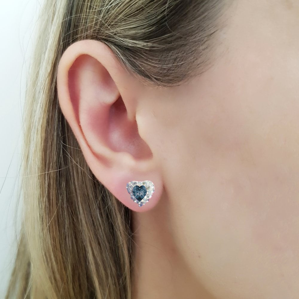Feminine heart stud earring with a dark blue montana heart crystal in the center (the birthstone for December), on a women ear. The heart shaped stud earring in sterling silver for pierced ears, with a deep denim blue central heart crystal and tiny moonlight crystals around it, in a pave style heart earring, made in Ireland by Lavinia of Magpie Gems Jewellery in Cork.