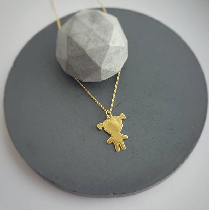 Elegant 24k gold plated little girl pendant necklace presented on a circular grey concrete backdrop, emphasizing the simple beauty of the piece.