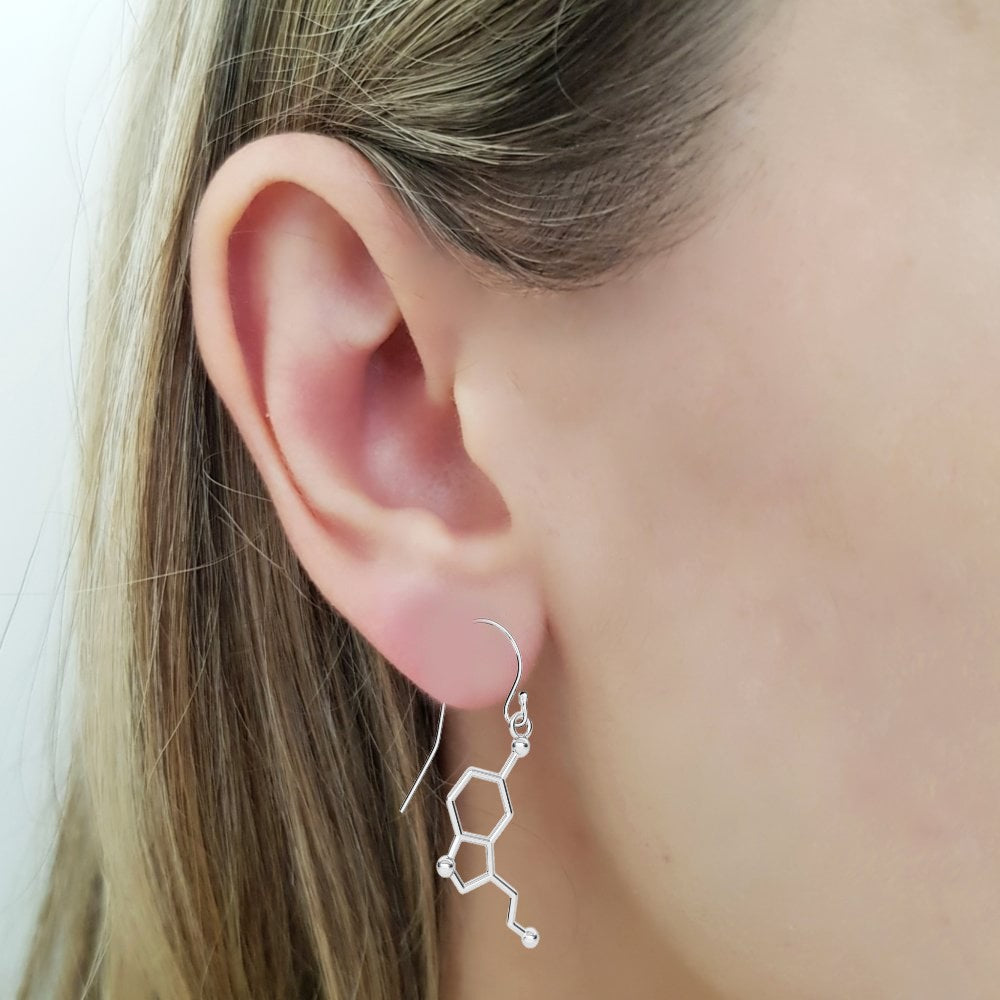 Women wearing a pair of silver earrings in the form of the serotonin molecule, a neurotransmitter that promotes emotions of happiness, satisfaction, and relaxation. The serotonin molecule served as the inspiration for these sterling silver 'Be Happy' earrings, in sterling silver for sensitive ears (no nickel). 