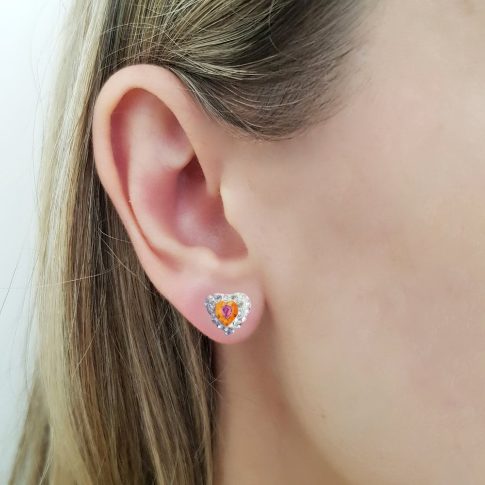 Dainty heart stud earring with a padparascha sapphire heart crystal in the centre (the birthstone for September), on a women ear. The heart shaped stud earring in sterling silver for pierced ears, with a vibrant orange with shades of pink central heart crystal and tiny moonlight crystals around it, in a pave style heart earring, made in Ireland by Lavinia of Magpie Gems Jewellery in Cork.