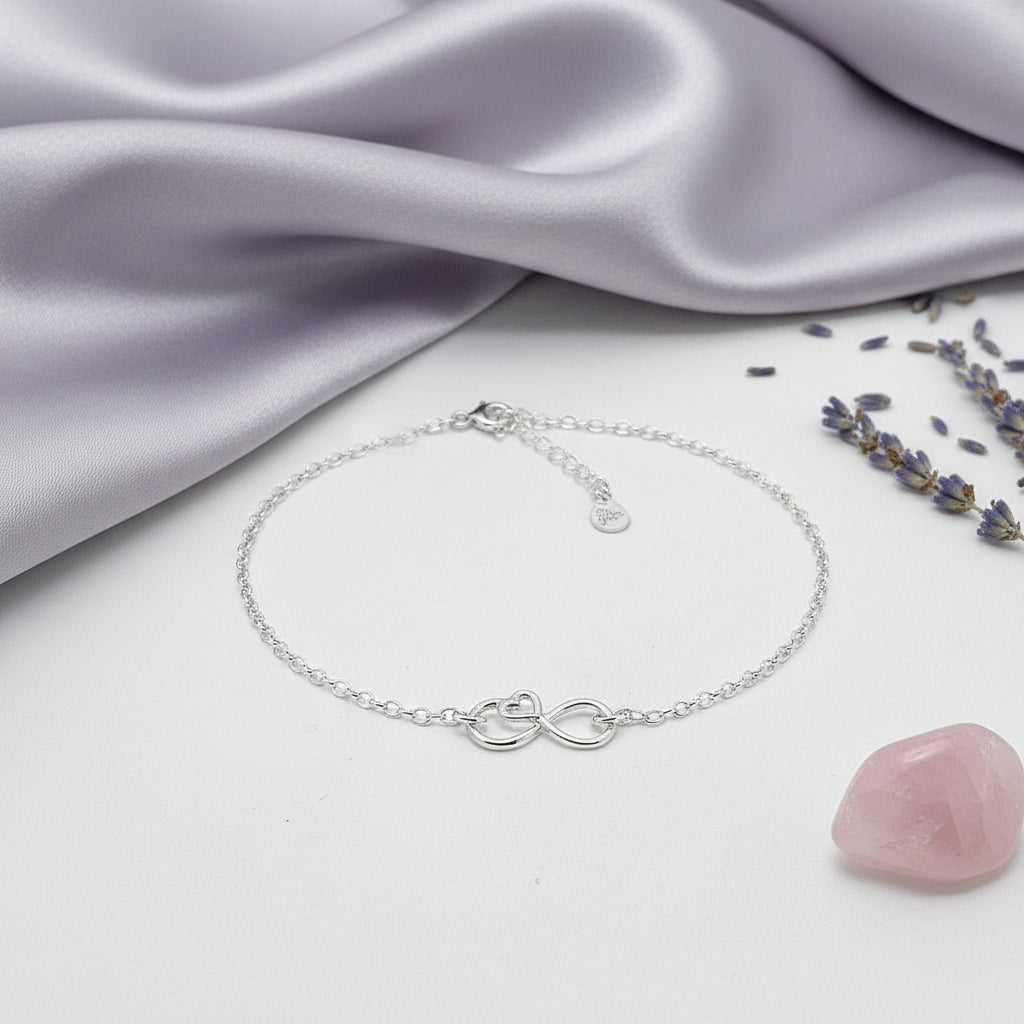 Silver bracelet with infinity symbol and love heart on a white surface with lavender and a pink stone.